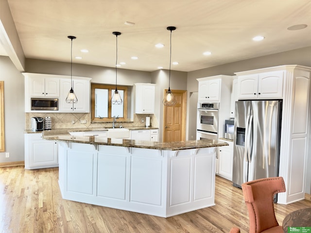 kitchen with dark stone countertops, decorative light fixtures, stainless steel appliances, and a kitchen island