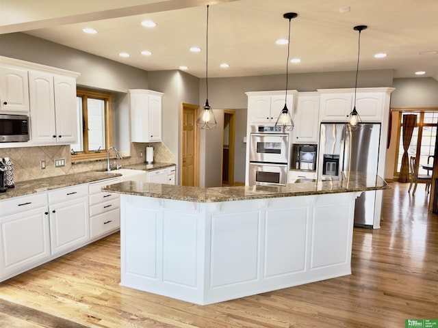 kitchen featuring stainless steel appliances, hanging light fixtures, a kitchen island, and white cabinets