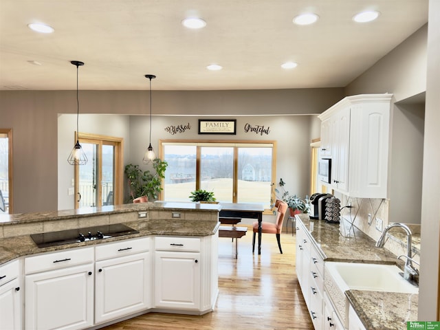 kitchen featuring pendant lighting, white cabinetry, dark stone counters, black electric stovetop, and light hardwood / wood-style floors