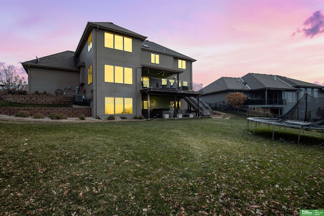 back house at dusk featuring a trampoline, a lawn, and a deck