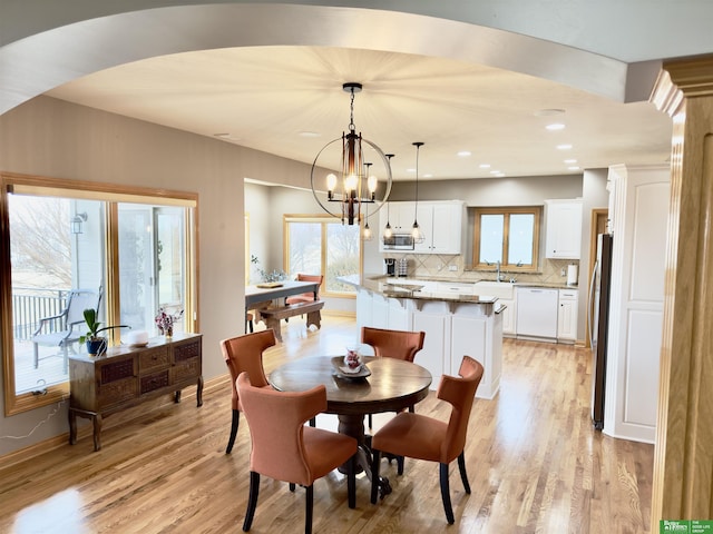 dining space featuring an inviting chandelier, a healthy amount of sunlight, sink, and light hardwood / wood-style flooring