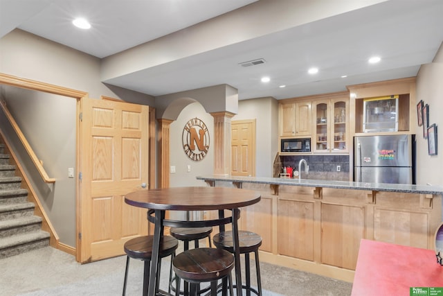 kitchen featuring stainless steel refrigerator, decorative columns, black microwave, light brown cabinets, and light carpet