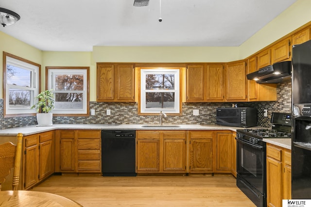 kitchen with sink, backsplash, range hood, black appliances, and light hardwood / wood-style floors