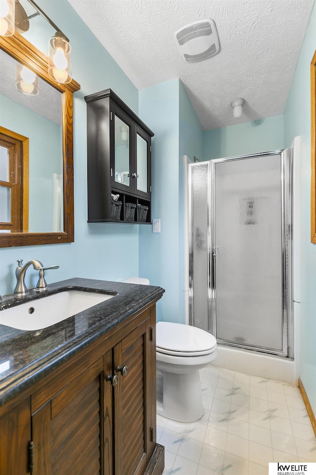 bathroom featuring vanity, toilet, a shower with shower door, and a textured ceiling