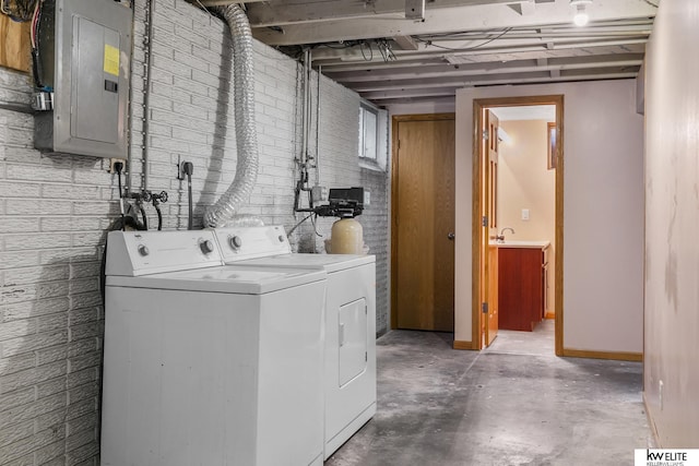 clothes washing area with washing machine and clothes dryer, brick wall, and electric panel