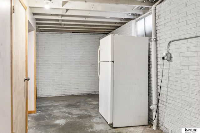 basement featuring brick wall and white fridge