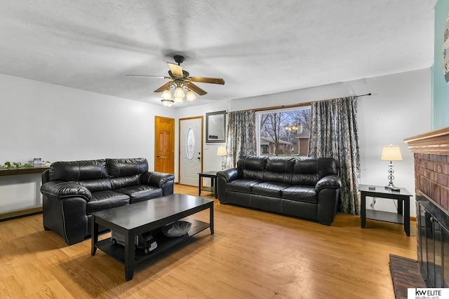 living room featuring a brick fireplace, a textured ceiling, light hardwood / wood-style floors, and ceiling fan