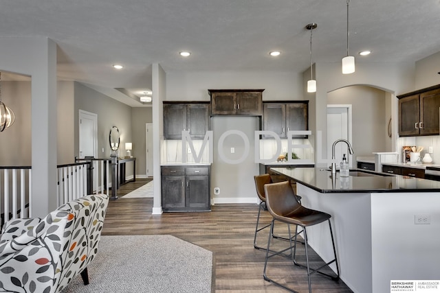 kitchen featuring sink, hanging light fixtures, dark hardwood / wood-style floors, dark brown cabinetry, and an island with sink