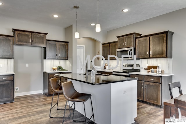 kitchen with sink, a center island with sink, hardwood / wood-style flooring, appliances with stainless steel finishes, and pendant lighting