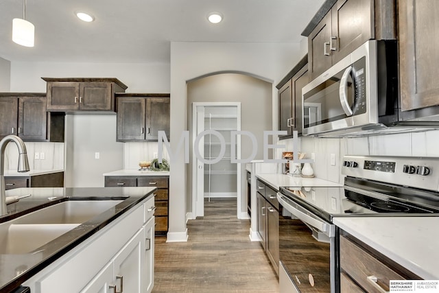 kitchen featuring sink, white cabinetry, stainless steel appliances, dark brown cabinetry, and decorative light fixtures