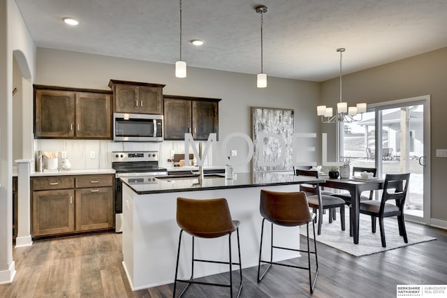 kitchen featuring hanging light fixtures, an island with sink, appliances with stainless steel finishes, and dark hardwood / wood-style flooring