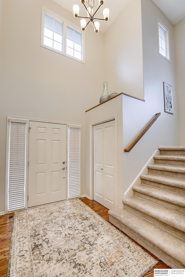 foyer entrance with hardwood / wood-style flooring, a towering ceiling, and a notable chandelier