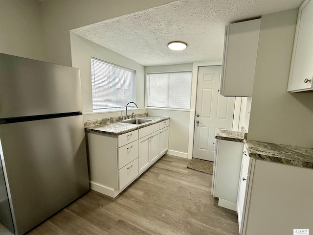 kitchen with sink, stainless steel fridge, light hardwood / wood-style flooring, white cabinetry, and a textured ceiling