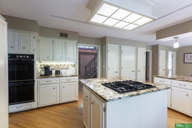 kitchen with pendant lighting, light stone countertops, black appliances, white cabinets, and a kitchen island