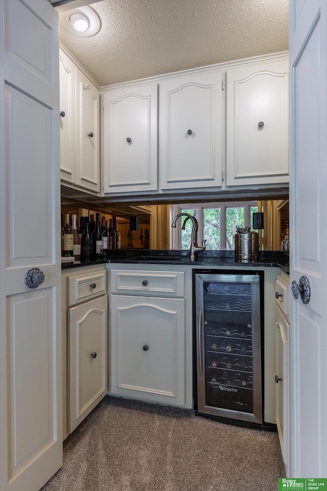 bar with a textured ceiling, beverage cooler, white cabinets, and carpet