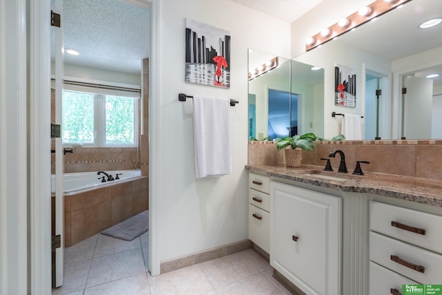 bathroom with tile patterned floors, vanity, a textured ceiling, and tiled tub