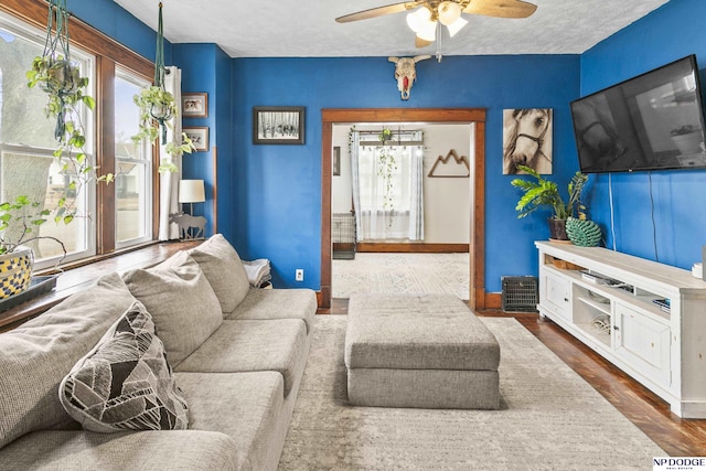 living room with ceiling fan, a textured ceiling, dark wood-type flooring, and a healthy amount of sunlight