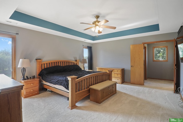 carpeted bedroom with multiple windows, a raised ceiling, and ceiling fan