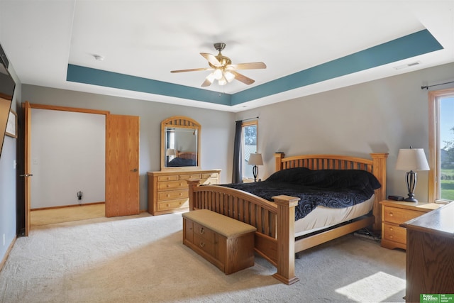 bedroom featuring ceiling fan, light colored carpet, and a raised ceiling