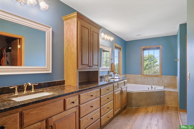 bathroom featuring hardwood / wood-style flooring, vanity, and tiled tub