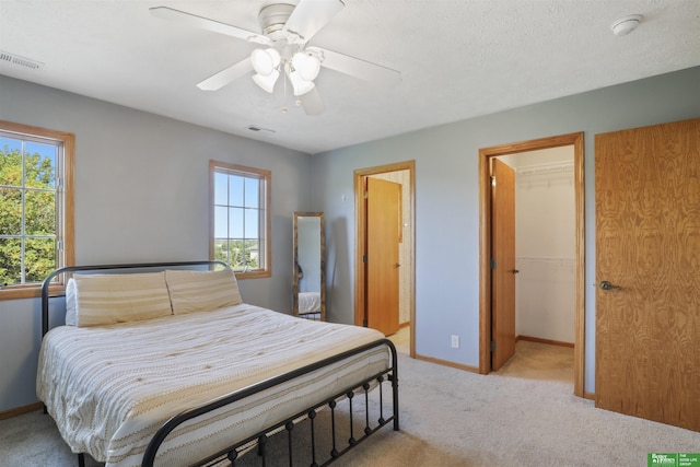 bedroom with ceiling fan, light carpet, multiple windows, and a walk in closet