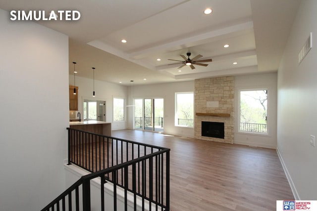 living room with a fireplace, light hardwood / wood-style flooring, a raised ceiling, and ceiling fan