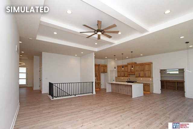 unfurnished living room with ceiling fan, light hardwood / wood-style floors, sink, and a raised ceiling