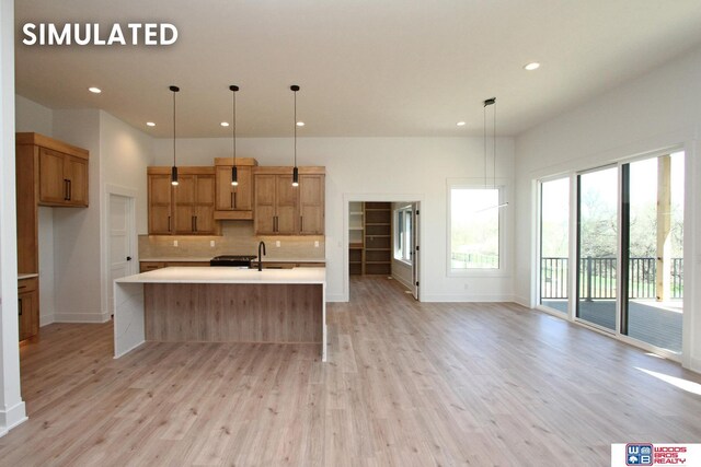 kitchen with tasteful backsplash, sink, hanging light fixtures, light hardwood / wood-style floors, and a spacious island