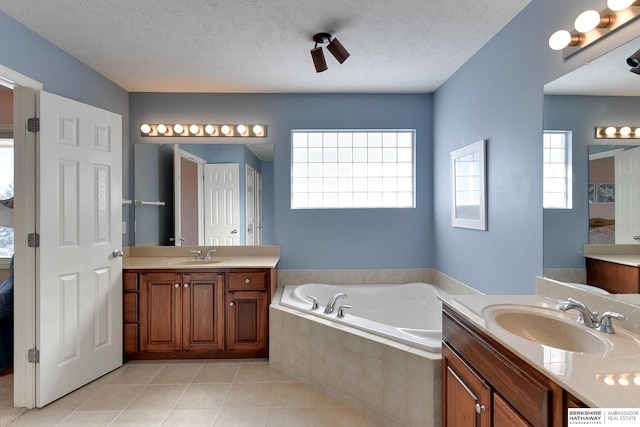 bathroom with a relaxing tiled tub, vanity, tile patterned flooring, and a textured ceiling