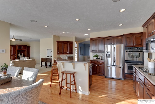 kitchen with a breakfast bar area, a kitchen island with sink, stainless steel appliances, light hardwood / wood-style floors, and backsplash