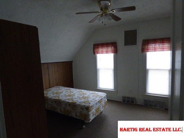 carpeted bedroom with ceiling fan, vaulted ceiling, and multiple windows