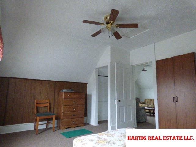 carpeted bedroom featuring multiple closets, lofted ceiling, and wooden walls