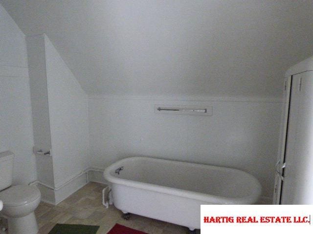 bathroom featuring lofted ceiling, toilet, and a bathing tub