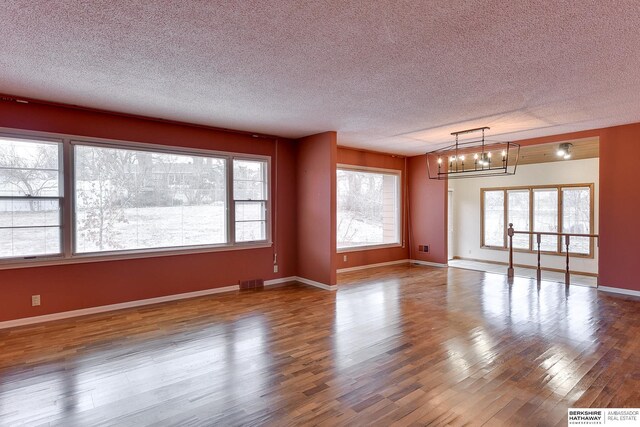 unfurnished room featuring hardwood / wood-style flooring, a chandelier, and a textured ceiling