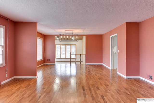 unfurnished room featuring a chandelier, a textured ceiling, and light hardwood / wood-style floors