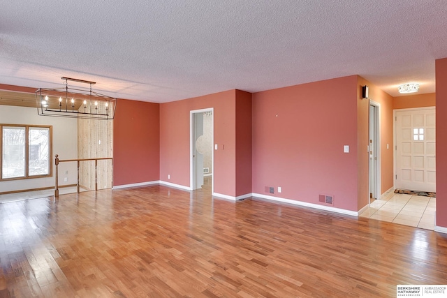 spare room with an inviting chandelier, light hardwood / wood-style flooring, and a textured ceiling