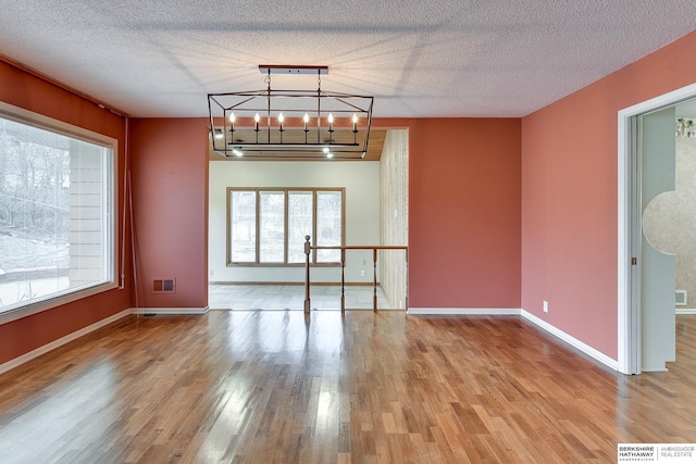 spare room featuring hardwood / wood-style floors, a textured ceiling, and an inviting chandelier