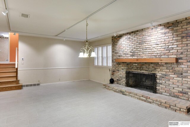 unfurnished living room featuring a brick fireplace, track lighting, and a chandelier