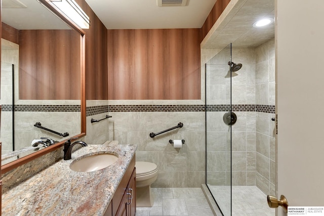 bathroom featuring vanity, toilet, tile walls, and a tile shower