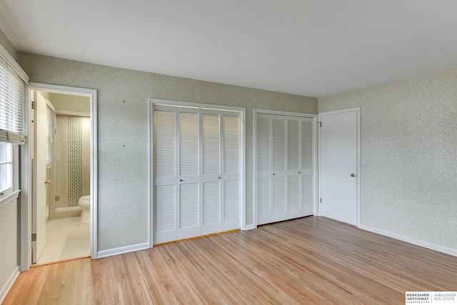 unfurnished bedroom with ensuite bath, multiple closets, and light wood-type flooring