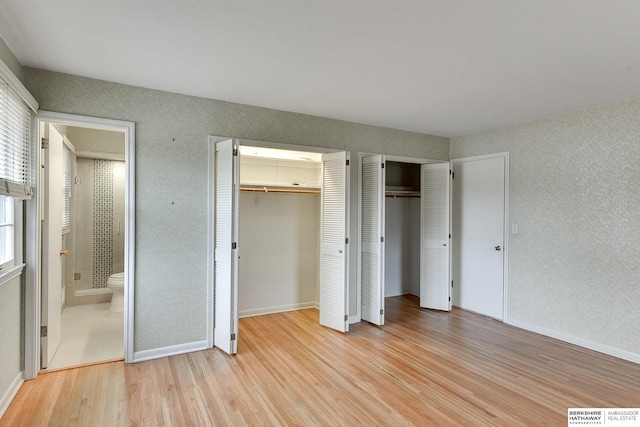 unfurnished bedroom featuring two closets, ensuite bath, and light wood-type flooring