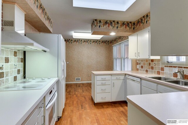 kitchen with sink, kitchen peninsula, white appliances, wall chimney range hood, and white cabinets