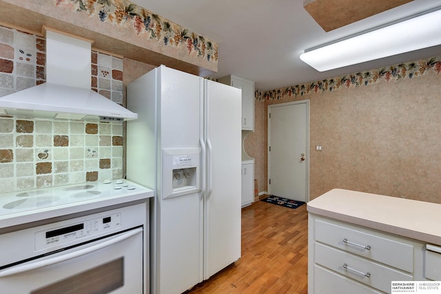 kitchen with wall chimney range hood, white cabinets, white appliances, and light hardwood / wood-style floors