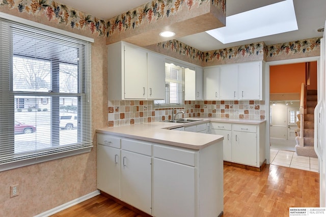 kitchen featuring white cabinetry, a skylight, sink, and light hardwood / wood-style flooring