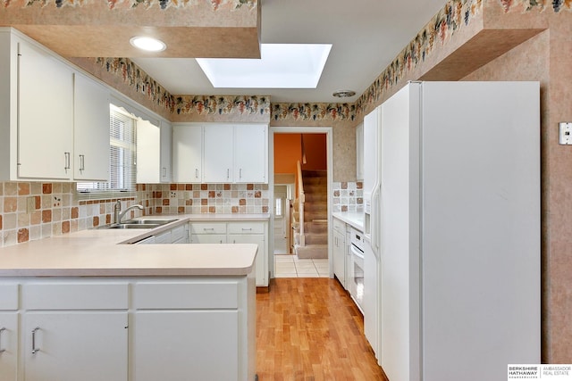 kitchen featuring white appliances, a skylight, sink, and white cabinets