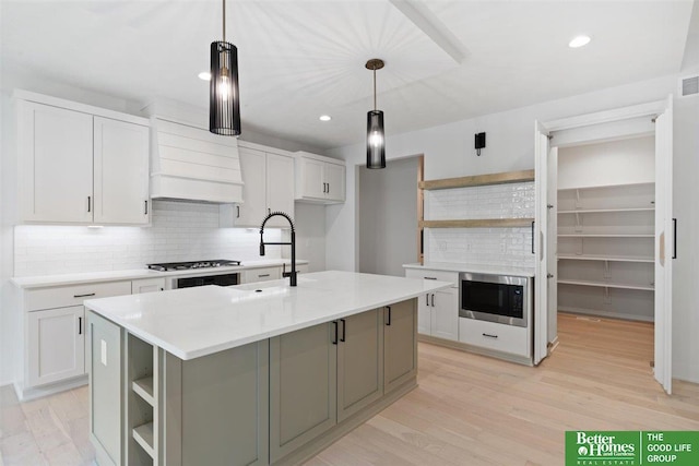 kitchen featuring built in microwave, sink, a kitchen island with sink, and white cabinets