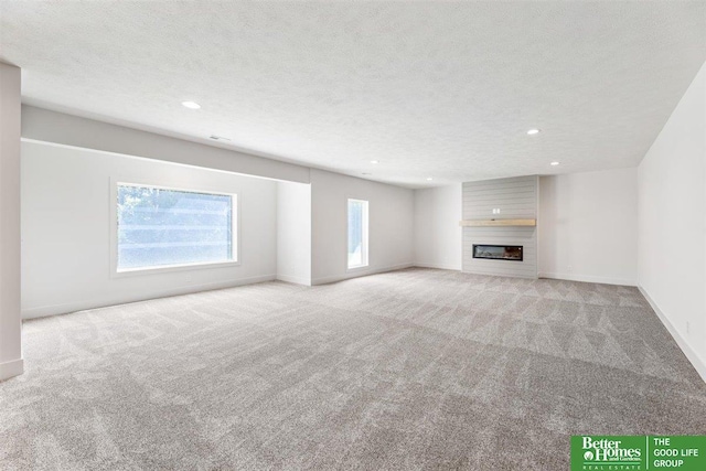 unfurnished living room featuring a large fireplace, light carpet, and a textured ceiling