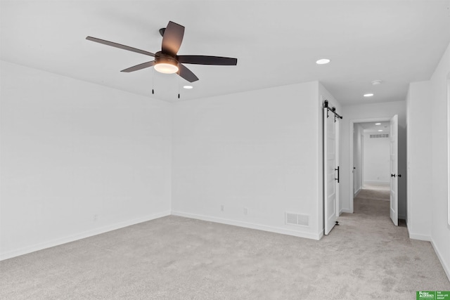 carpeted spare room featuring ceiling fan and a barn door