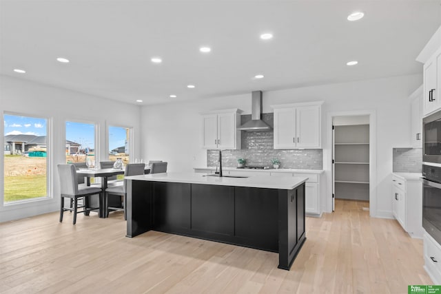 kitchen with sink, white cabinets, a kitchen island with sink, wall chimney exhaust hood, and light hardwood / wood-style flooring