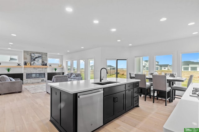 kitchen with dishwasher, an island with sink, a large fireplace, sink, and light hardwood / wood-style floors